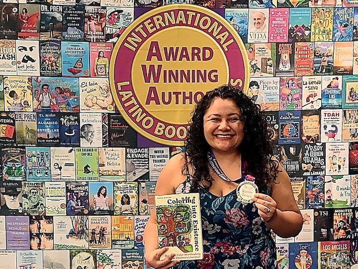 Isabel Millán stands in front of a poster of book covers holding her book